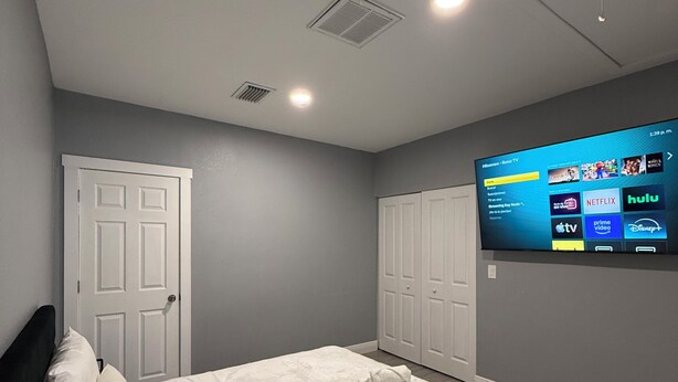 A bedroom with a bed, two white doors, a television mounted on the wall, and a ceiling with recessed lighting. - Private 1BR Suite, Free Parking, Near Downtown & Airport (Tampa)