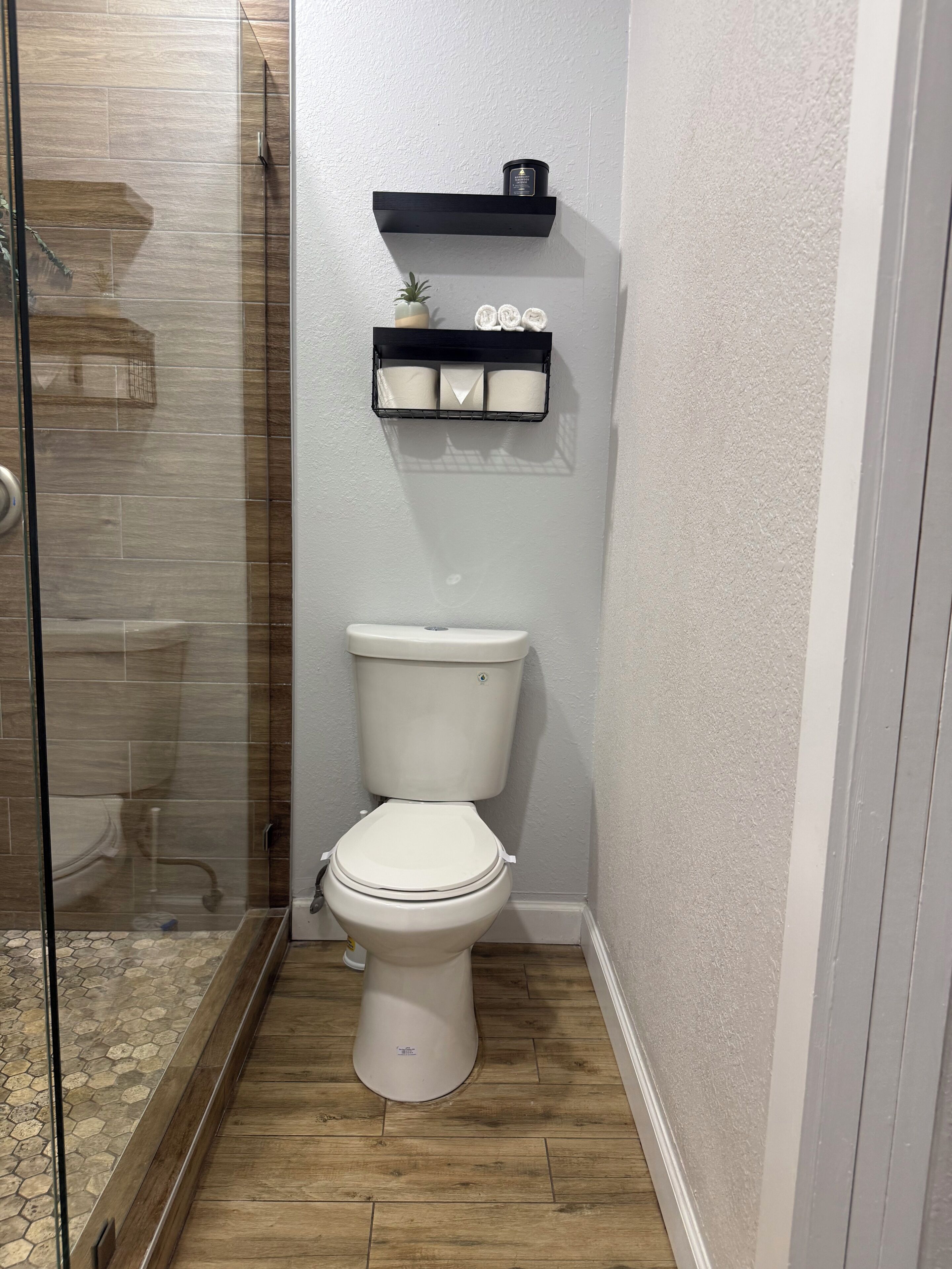 Een badkamer met een douchecabine van glas, een toilet en een plank met kaarsen en een klein plantje.