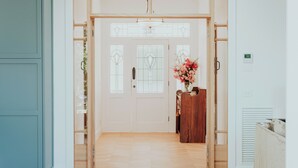 Un pasillo con una puerta de madera, un pequeño escritorio de madera con un florero y un radiador a la derecha.