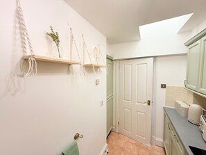 Ein Badezimmer mit weißer Tür, Handtuchhalter, Waschbecken mit Ablagefläche und einem Fenster darüber.