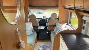 Un intérieur de camping-car compact comprenant un coin cuisine, un espace salon et une vue sur l’extérieur.