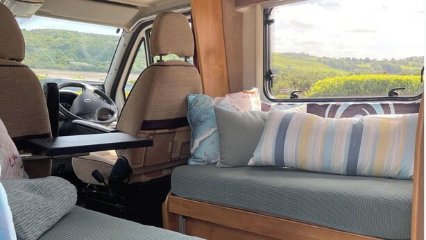 L'intérieur d'un camping-car est aménagé avec une table à manger, des sièges rembourrés et offre une vue sur un paysage verdoyant.