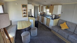 Interior compacto de um veículo recreativo, com cozinha compacta, área de refeições e espaço para sentar.
