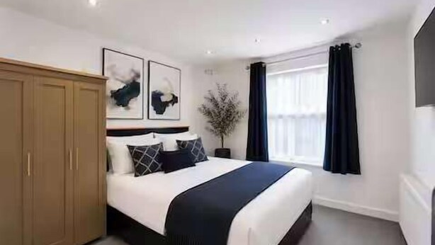 A bedroom with a bed, a wardrobe, and a window with curtains. - Nottingham Home 4 Bedrooms sleeps 7 city hospital (Nottingham)