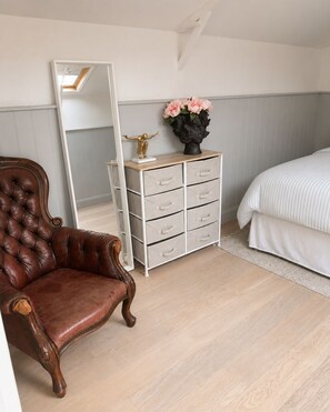 A bedroom with a large mirror, a wooden chair, a dresser with drawers, and a bed with a striped bedspread. - Waterside studio on River Thames (Hampton)