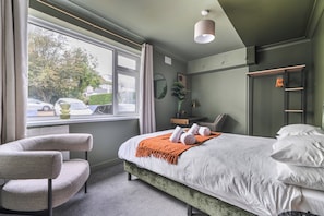 A hotel room with a bed, a chair, a window with curtains, a bedside table, and a mirror. - 2 Bed Apartment Sleeps 4 - Pets Welcome (St. Ives)