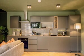 Eine moderne Küche mit grauen Schränken, einer Edelstahl-Dunstabzugshaube, einem eingebauten Backofen und einer Arbeitsplatte mit Wasserkocher und Toaster.