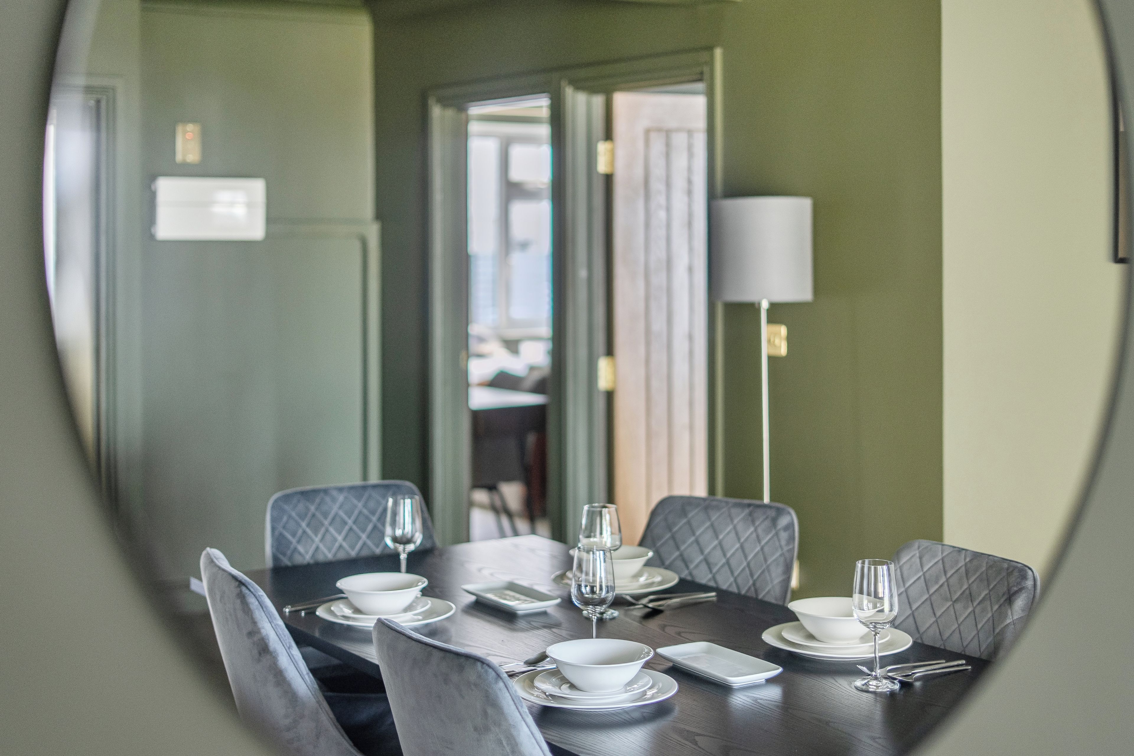 Un coin repas avec une table ronde dressée pour quatre personnes, agrémentée d’assiettes, de bols et de couverts blancs.