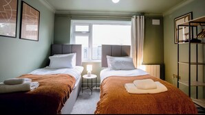 A double room with two beds, a window, a small table, and a wardrobe. - 2 Bedroom Apartment Sleeps 3 - Garden - Pets (St. Ives)