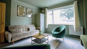 A living room with a sofa, a coffee table, a chair, and a window with curtains. - 2 Bedroom Apartment Sleeps 3 - Garden - Pets (St. Ives)