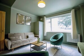 Ein Wohnzimmer mit Sofa, Couchtisch, Stuhl und einem Fenster mit Vorhängen.