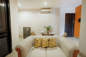 Ein Wohnzimmer mit einer Couch, einem Esstisch mit Stühlen, einer Klimaanlage und einem Kühlschrank.