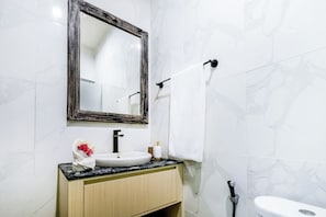 Ein Badezimmer mit weißem Waschbecken, einem Spiegel mit Holzrahmen, einem Handtuchhalter und einer Toilette.