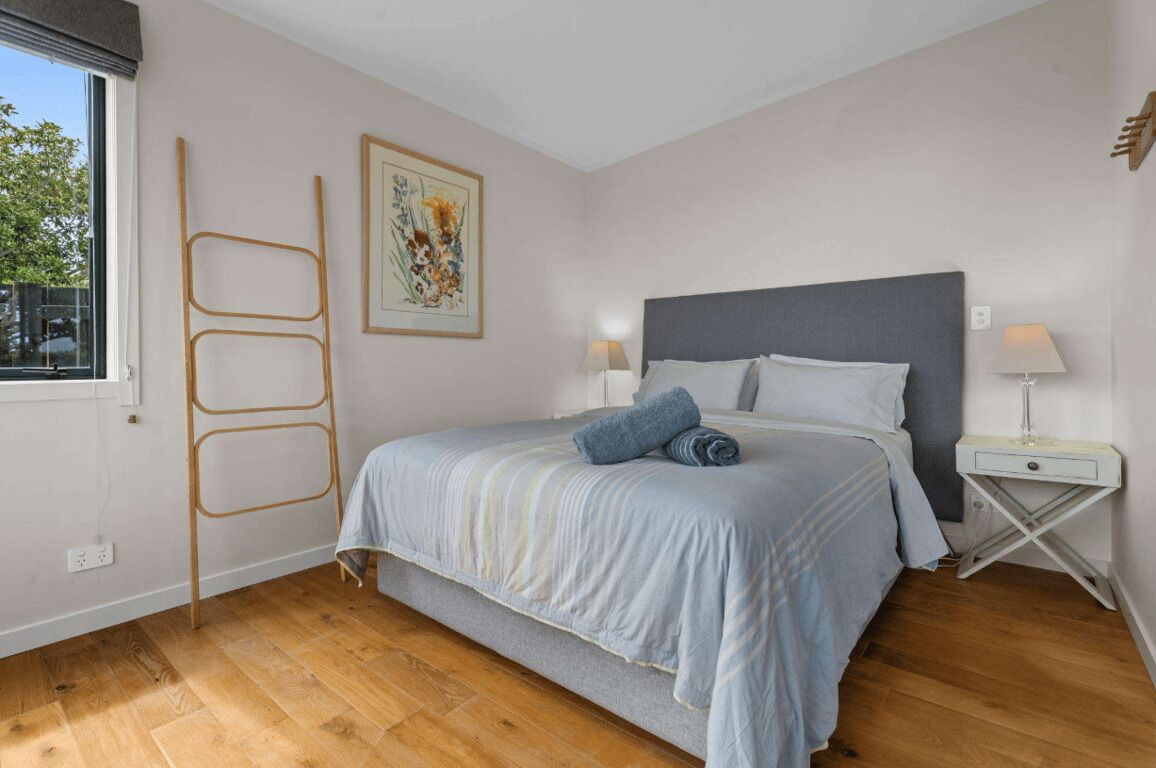 Ein Schlafzimmer mit einem Bett, Nachttischen, einem Fenster und Holzboden.