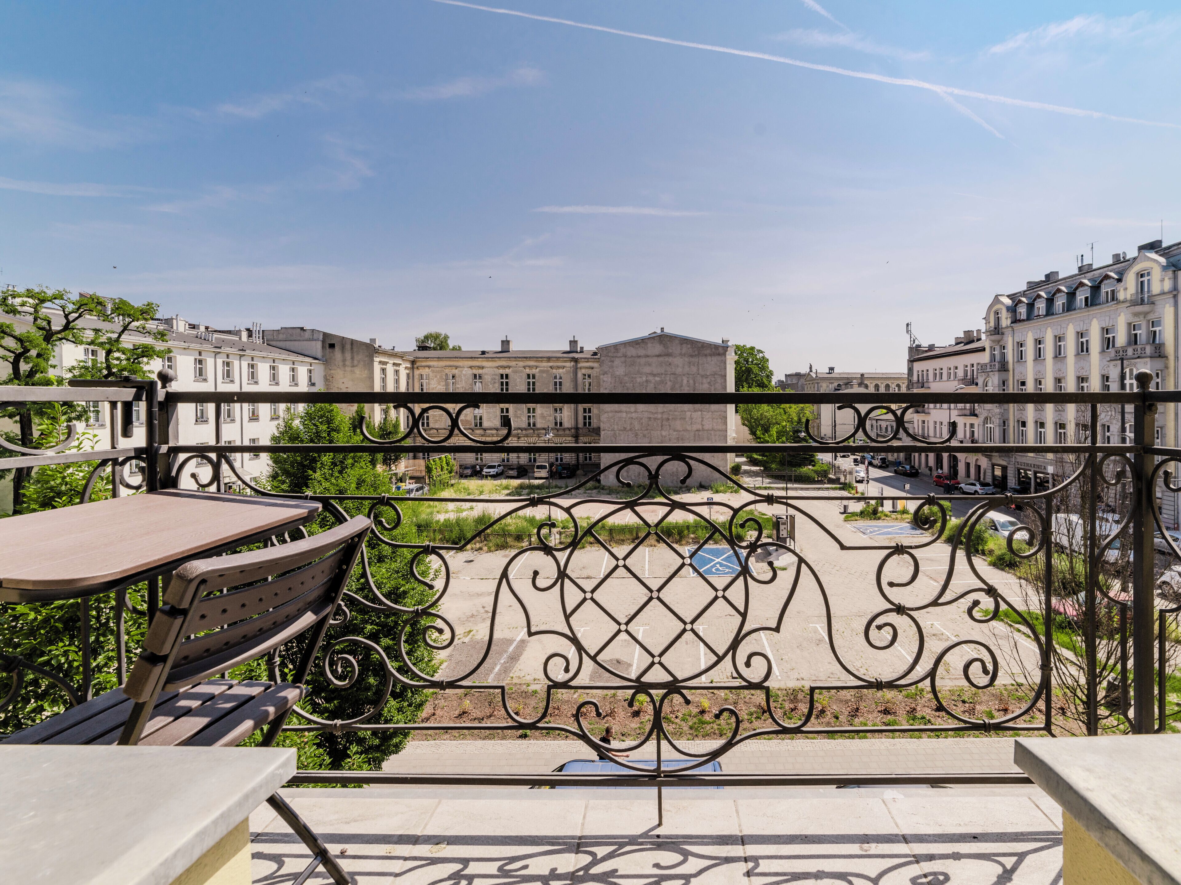 A balcony with a table and chairs, overlooking a cityscape with historic buildings and a clear sky.