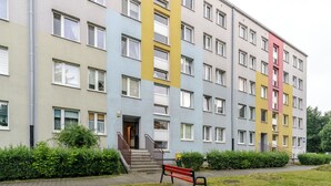 Ein mehrgeschossiges Wohngebäude mit einer zentralen Treppe, einer roten Bank und einem gepflegten Rasen.