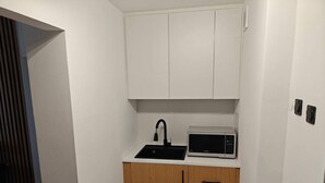 A compact kitchenette with a microwave, sink, and wooden cabinets. - Grajewo Modern Apartment (Grajewo)
