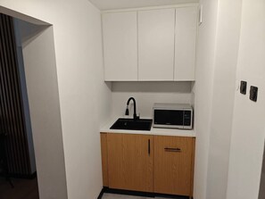A compact kitchenette with a microwave, sink, and wooden cabinets.