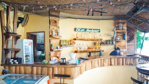 A bar area with a wooden counter, shelves with bottles, a fan, and a refrigerator. - Blue Harbour Phuket  (Patong)