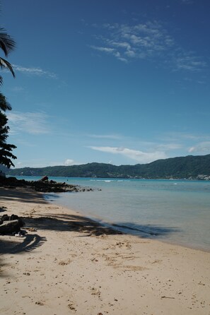 A beach with clear skies, calm water, and a distant mountain range. - Blue Harbour Phuket (Patong)