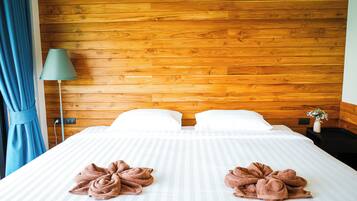 Quarto de hotel com cabeceira de madeira, cama com lençóis brancos, duas toalhas castanhas, abajur verde e cortina azul.