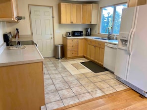 A compact kitchen with wooden cabinets, a microwave, a sink, and a refrigerator. - The Server: Main Guest Suite (Lynnwood)
