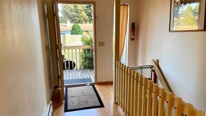 A hallway with a wooden floor, a black mat at the entrance, and a wooden railing on the right.