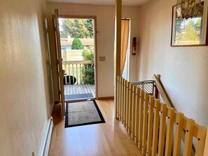 A hallway with a wooden floor, a black mat at the entrance, and a wooden railing on the right. - The Server: Main Guest Suite (Lynnwood)