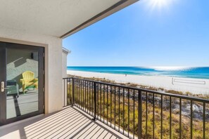 Ein Balkon mit Blick auf einen Strand, eine Tür mit Glasfenster und ein gelber Stuhl.