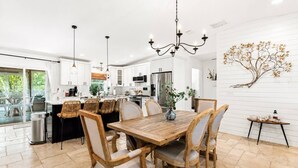 A modern kitchen with white cabinets, a wooden dining table, wicker chairs, and a chandelier. - Luxury Retreat |Pool| Game Room|Billards|AirHockey (St. Augustine)