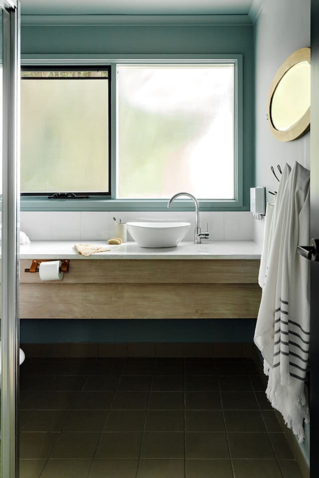 A bathroom with a large window, a white sink, and a wooden vanity.