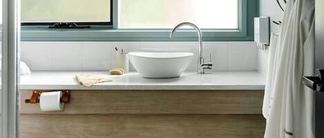 A bathroom with a large window, a white sink, and a wooden vanity.