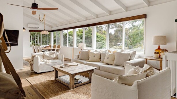 A spacious living room with a large window, a ceiling fan, and a fireplace. - The Mariner by Experience Metung (Metung)