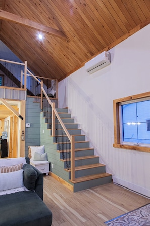 Una escalera con escalones de madera y barandillas de metal, una pared blanca con una ventana y un techo de madera.