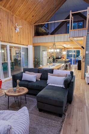 A modern living room with a sectional sofa, a dining area, and a kitchen visible through an open door.