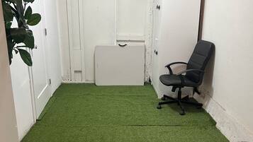 A room with a green artificial turf floor, a white door, a black office chair, and a white cabinet.