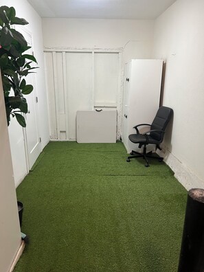 Una habitación con piso de césped artificial verde, una puerta blanca, una silla de oficina negra y un armario blanco.