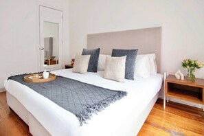 A neatly made bed with a grey blanket, a bedside table with a vase of flowers, and a wooden tray with a cup and a pastry. - Casa Corazón | 5BR Oasis in La Condesa (Mexico City)