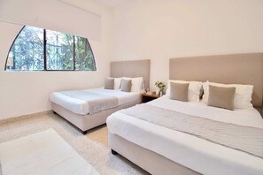 A hotel room with a large bed, a smaller bed, a nightstand, and a window with a view of trees. - Casa Corazón | 5BR Oasis in La Condesa (Mexico City)