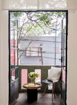 A balcony with a chair, a small table with a vase, and a view of the street and buildings. - Casa Corazón | 5BR Oasis in La Condesa (Mexico City)