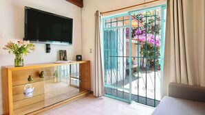 A room with a TV mounted on the wall, a wooden console table with drawers, a glass display cabinet, a sofa, and a sliding glass door leading to an outdoor area with a metal gate and pink flowers. - Geodesic sanctuary with a heated pool (Chiconcuac)