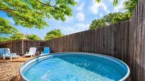 An outdoor swimming pool with a wooden fence, surrounded by lounge chairs and a wooden deck. - The Coop & Roost | Hot Tub & Cowboy Pool! (Fredericksburg)