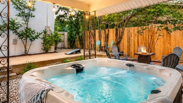 A hot tub with a safety sign, surrounded by wooden deck chairs and a wooden fence. - The Coop & Roost | Hot Tub & Cowboy Pool! (Fredericksburg)