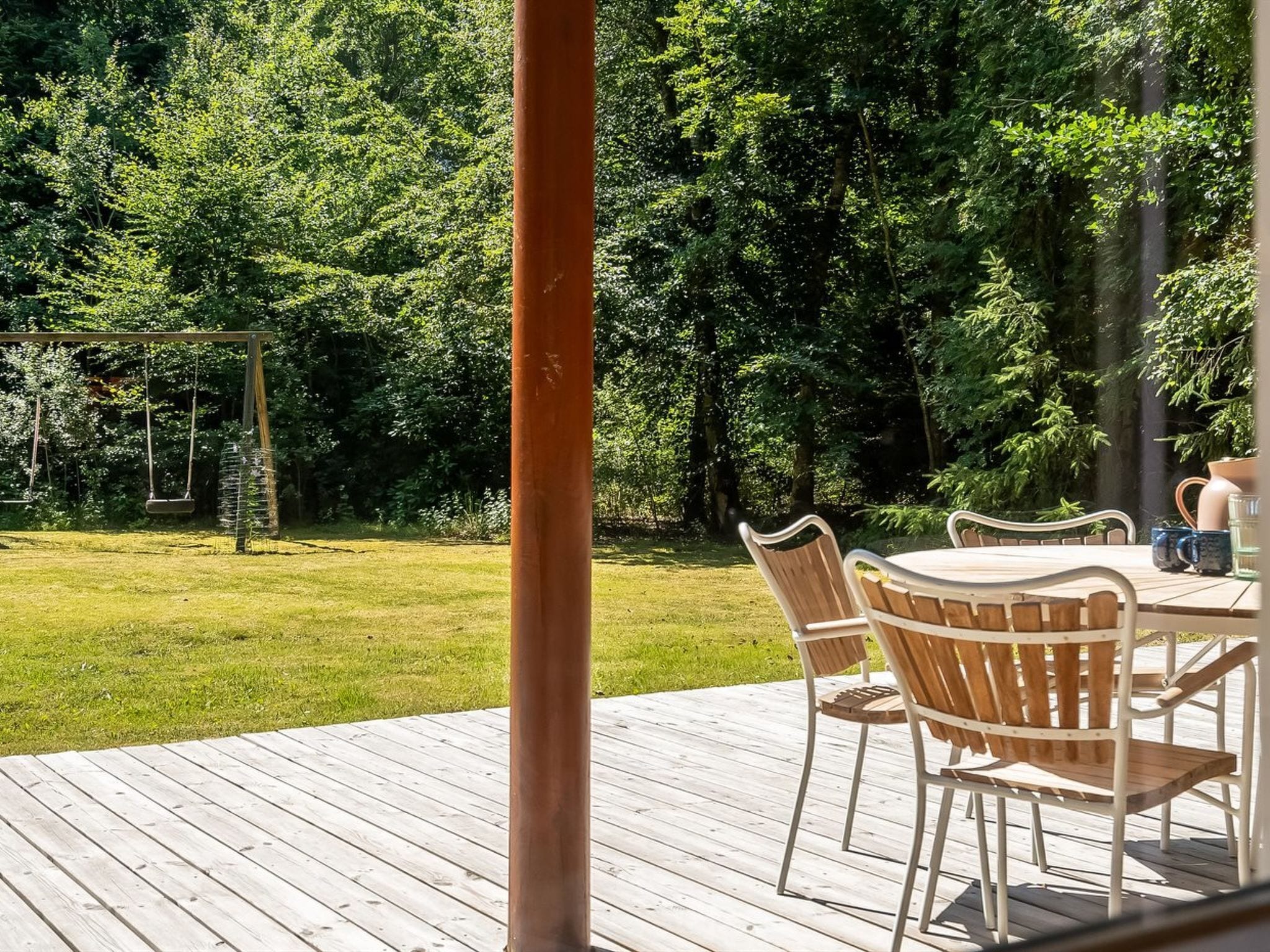 A wooden deck with a table and chairs, surrounded by a lush green garden.
