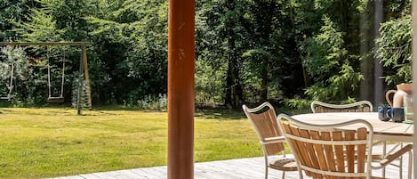 A wooden deck with a table and chairs, surrounded by a lush green garden.