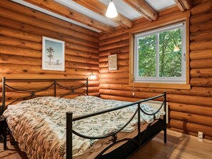 Una habitación de cabaña de madera con una cama, un ventanal con vistas a árboles y un cuadro en la pared.