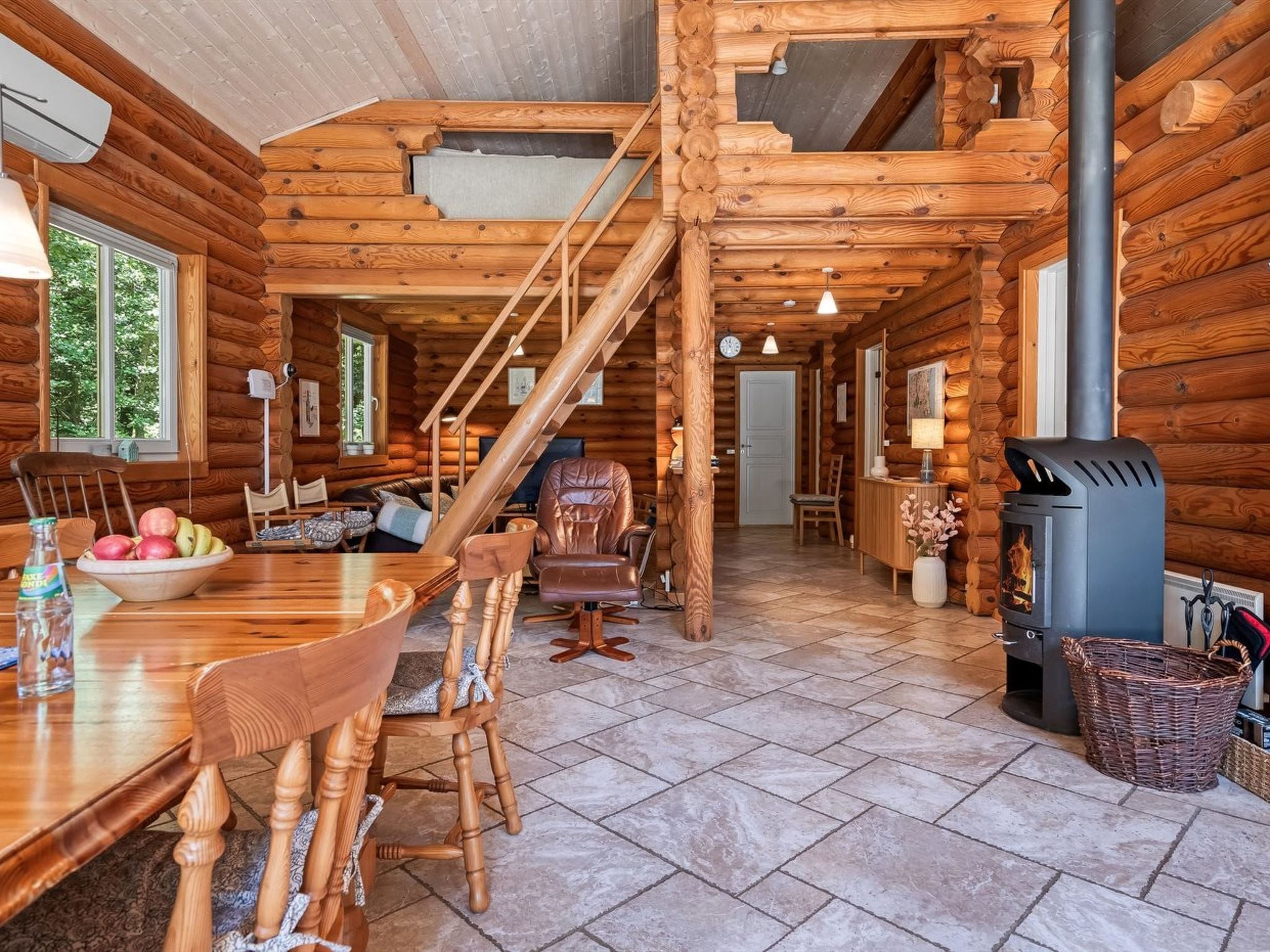 A log cabin interior with a dining area, a fireplace, and a staircase.