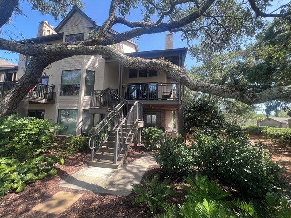 A two-story building with a central staircase, surrounded by lush greenery and trees. - Waterfront Marina Condo & Breathtaking Sunset Views & Walk to Dining (Johns Island)