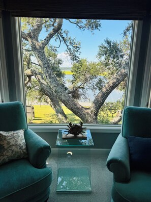 A room with two green armchairs facing a large window overlooking a tree and a body of water.