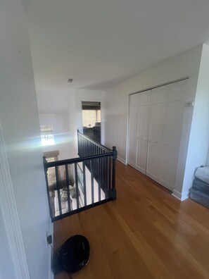 Ein Zimmer mit Holzboden, schwarzem Geländer, weißer Tür und einem Fenster.